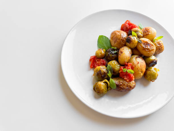 istock Roasted baby potatoes and Brussels sprouts with cherry tomatoes on white plate, garnished with basil, healthy vegetarian dish concept with space for text. 2053408547