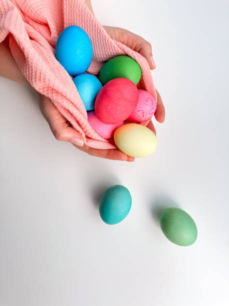 Hands cradling collection of brightly colored Easter eggs in pink fabric, evoking themes of Easter traditions, family fun, and springtime crafts.
