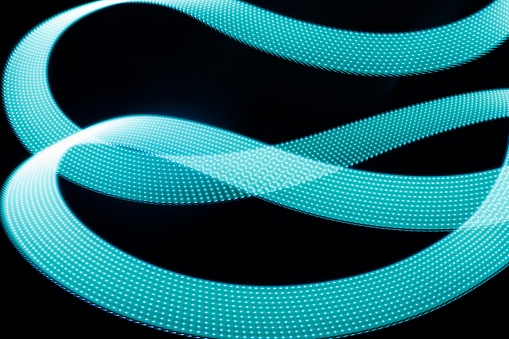 Turquoise blue glowing neon wave of light as curls or swirl with dotted stripes on black background, pattern. Abstract background with motion light effect in hipster style.