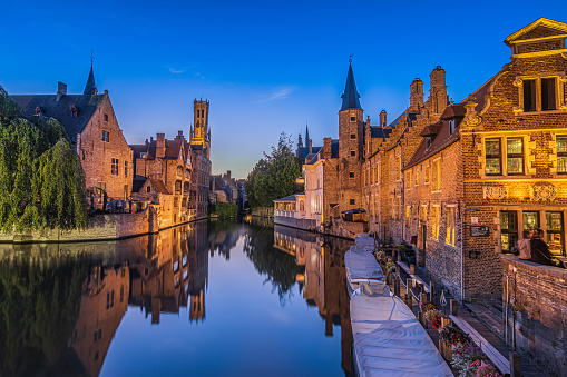 Rosary Quay in the Hanseatic city of Bruges. Reflection on the water surface of the canal of the historic buildings in the evening. Belfry tower of the old town and historic guild houses