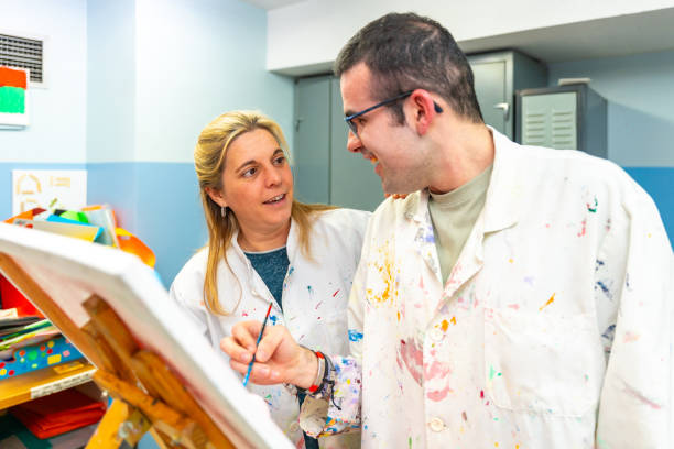 istock Teacher of a painting class talking to a disabled student 2053440481