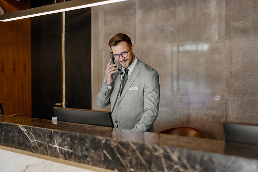 Receptionist talking on phone at desk in lobby. Hotel concierge.