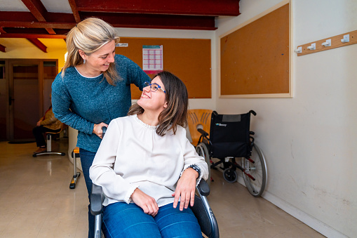 Caregiver pushing the wheelchair of a disabled woman in a day center for people with special needs