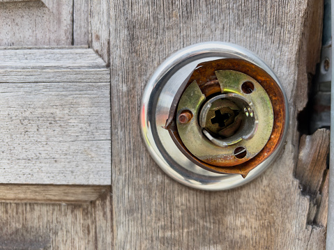 A weathered door knob on an aged wooden door.\nThe metal knob is partially rusted and reveals its inner mechanism, creating a contrast with the cracked and lined wood surface. This could be used for themes such as history, decay, mystery, or nostalgia.