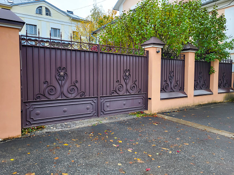Beautiful brown wrought iron gate and fence on the street against a tree background