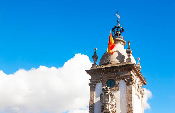 istock An ancient clock tower with a Spanish flag against a blue sky with white clouds. 2053560818