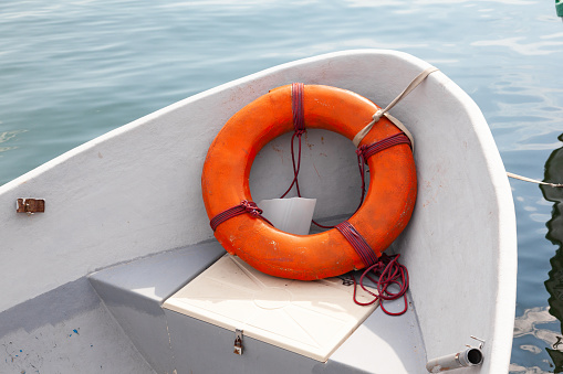 White wooden boat with an orange lifebuoy on the bow on the water.