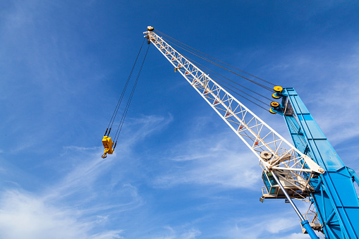 Top of port crane with a stabilizer and a hook against a blue sky.