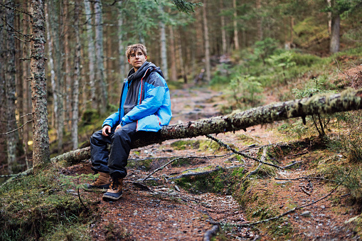 Teenage boy hiking in the alpine forest - Salzburg, Austria.
The boy is sitting on a tree trunk, lying across the path.
Shot with Canon R5