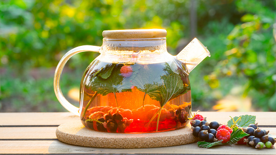 Berry tea brewed in a glass transparent teapot on a natural background