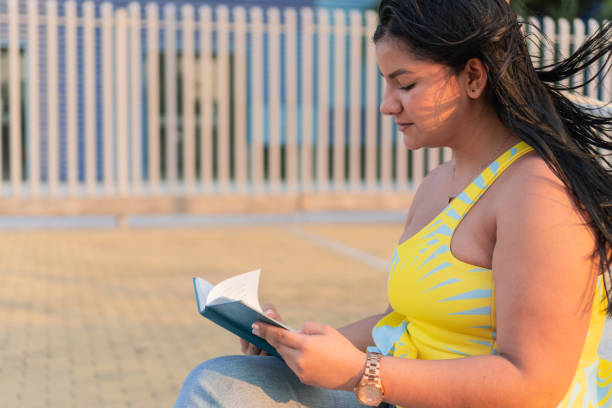 Woman engrossed in reading a book during sunset.