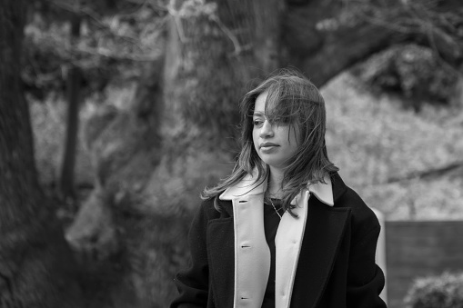 A vertical grayscale shot of a woman wearing a casual outfit and a beret posing outdoors