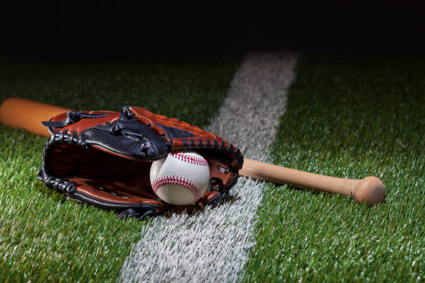 istock Baseball in a mitt with bat at low angle view on a field with stripe and dramatic lighting and dark background 2053631068