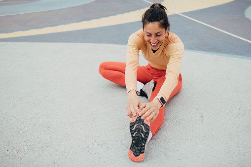 Smiling woman in sportswear stretching on a colorful outdoor court, conveying health, fitness, and happiness.