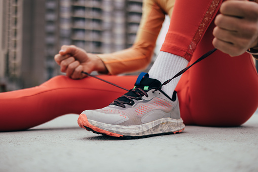 Close-up of athlete tying running shoe laces, preparing for a jog, with focus on fitness and determination.