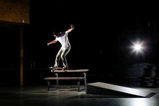 Skateboarder doing a skate trick/stunt on a skatepark obstacle. This image was shot with controlled lighting and has a high contrast/low key tone to it.