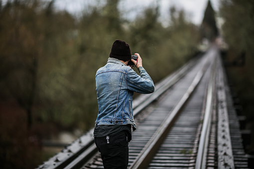 Unrecognizable Male Figure exploring railroad tracks in the Pacific Northwest. He is wearing a black beanie and faded blue denim jacket.