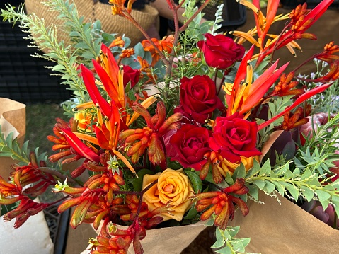 High angle closeup photo of a beautiful colourful bunch of mixed flowers and Wattle leaves on stems, on display for sale on a stall at the Byron Bay Farmers Market in Summer.