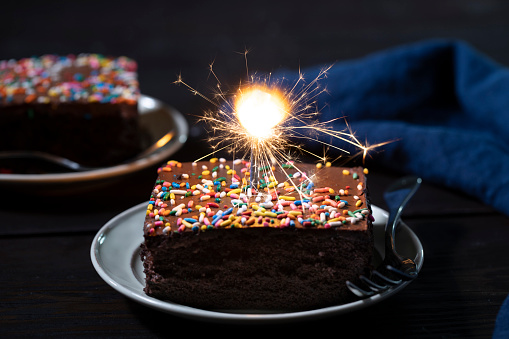 Colorful birthday cake with sprinkles and burning star shaped candles on a dark wall background. Festive birthday celebration, party. Selective focus, copy space