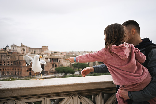 Family feeding seagull on terrace with panoramic view on ancient Rome.
