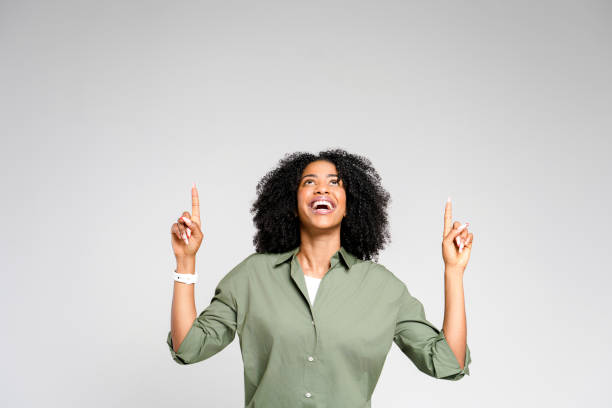 istock A joyful African-American woman points upward with both hands, looking delighted with her discovery 2053899783