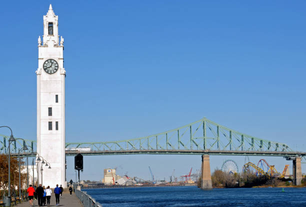 Montreal, QC, Canada, Nov. 8, 2023: The historic clock tower in Montreal's Old Port was completed in 1922 as a memorial to sailors lost in the First World War. Behind it is the Jacques Cartier Bridge and La Ronde amusement park.