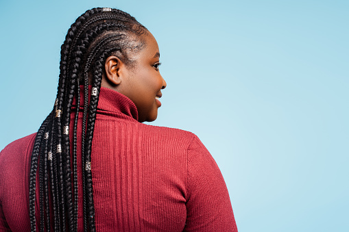 Back view portrait smiling African American woman with stylish braided hair looking away. Happy fashion model posing isolated on blue background, copy space. Customer, hair salon concept
