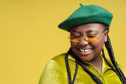 Closeup portrait smiling stylish African American woman wearing sunglasses, french beret isolated on background, copy space. Plus size fashion model posing in studio. Shopping, store, advertisement