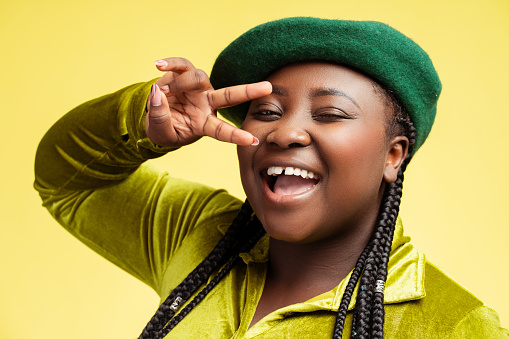 Portrait happy stylish African woman wearing green beret taking selfie showing victory sign isolated on background. Overjoyed blogger influence recording video. Cute fashion model posing in studio