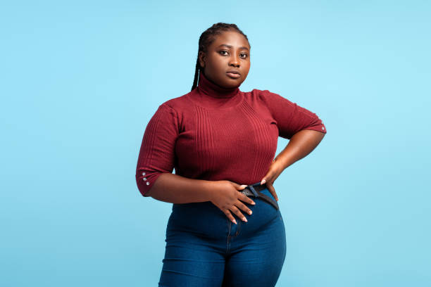 fashion portrait of serious african american woman wearing casual red sweater and denim - plussize model fotos stockfoto's en -beelden