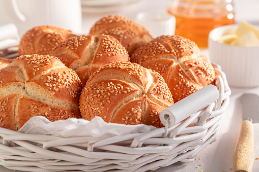 Sweet Kaiser rolls with sesame seeds served with drink. Breakfast with rollss, butter and honey.
