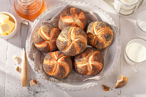 Homemade Kaiser buns with poppy seed in white basket. Breakfast with buns, butter and honey.