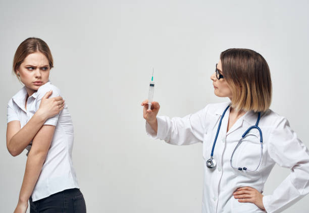 istock Frightened patient and nurse with a syringe in hand on a light background 2054090806