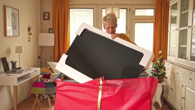 A happy woman is lifting a large new television from the Christmas wrapping
