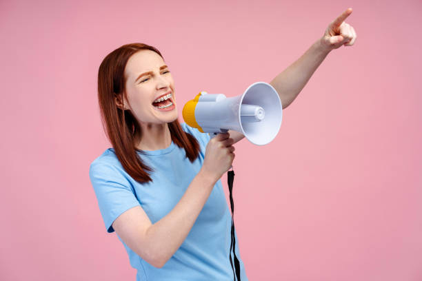 istock Red haired woman, energetically shouting through a loudspeaker, making a pointing gesture 2054160835