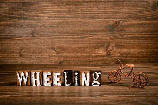WHEELING. Text from alphabet blocks and rusty miniature bicycle on wood texture background.