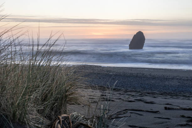 a rocky beach with a large rock in the foreground - beauty in nature cloud rocky coastline rock foto e immagini stock