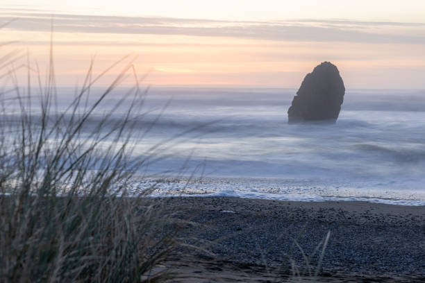 A rocky shoreline with a large rock in the foreground. The sky is a mix of orange and pink hues, creating a serene and peaceful atmosphere