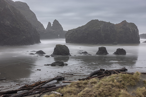 A rocky shoreline with a foggy, misty atmosphere. The rocks are scattered throughout the area, with some closer to the water and others further away. The scene is calm and peaceful