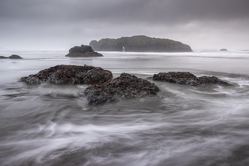 A rocky shoreline with a large rock in the foreground. The water is choppy and the sky is cloudy, creating a moody atmosphere