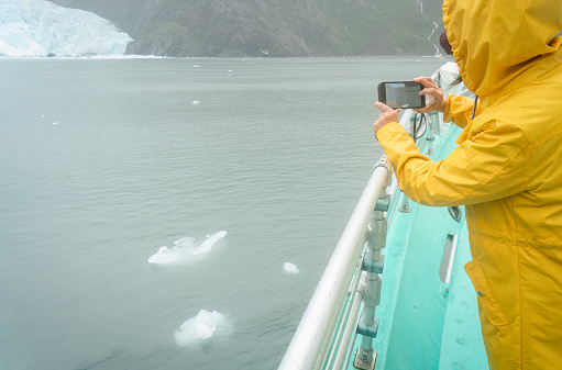 Woman taking photos of icebergs using smartphone. Holgate Glacier. Kenai Fjords National Park. Alaska.