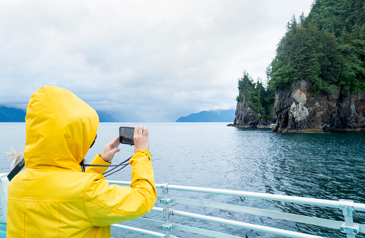 Tourist taking smartphone photos on the boat at Resurrection Bay, Kenai Fjords National Park, Seward, Alaska.