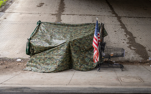 An American flag at a homeless tent made of camouflage tarp at a road underpass