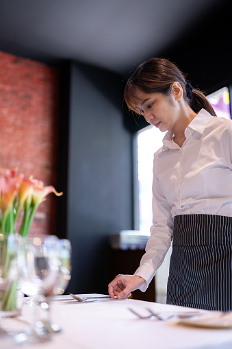 A waitress setting table in a restaurant before business starts