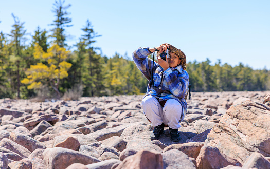 Woman tourist with camera exploring Boulder Field - Ice Age geological formation in Hickory Run State Park, Poconos region, Pennsylvania