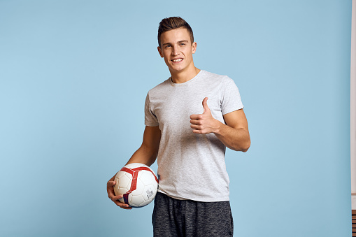 Happy guy with soccer ball in hand on blue background plays soccer cropped view. High quality photo