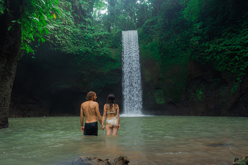 Young cheerful couple swimming in refreshing waterfall on Bali