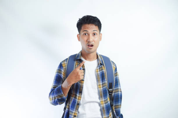 istock amazed young Asian student man with a backpack pointing at herself, shocked by sudden success isolated on white background 2054728639
