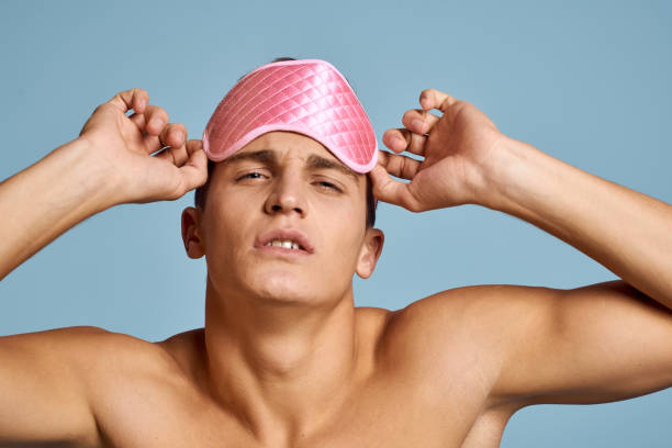 istock Relaxed man with pink sleep mask on blue background nude torso cropped view 2054729675