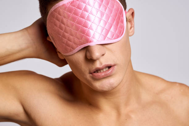 istock A man in a pink mask for sleeping on a light background at night gestures with his hands 2054731746